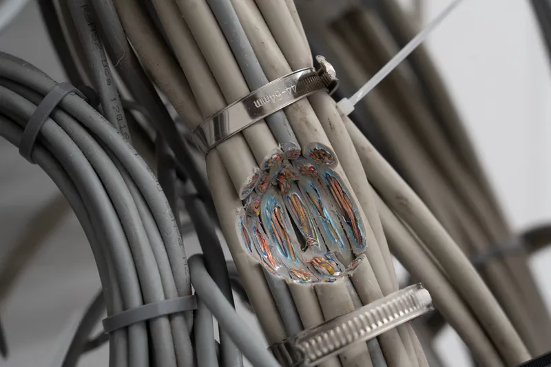 Close-up of grey cable bundles held by metal clamps around a glass object